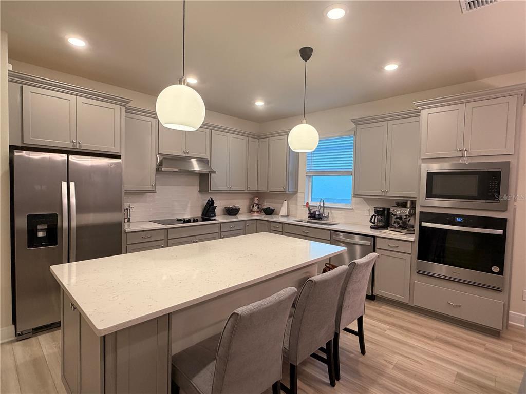 A modern kitchen features gray cabinetry, stainless steel appliances, and a large white island — 6024 FOREST PERCH DRIVE, ST CLOUD, FL
