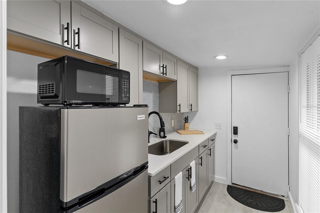 A small kitchen features gray cabinets, stainless steel appliances, a sink, and a white door — 412 E HARWOOD STREET UNIT 2, ORLANDO, FL