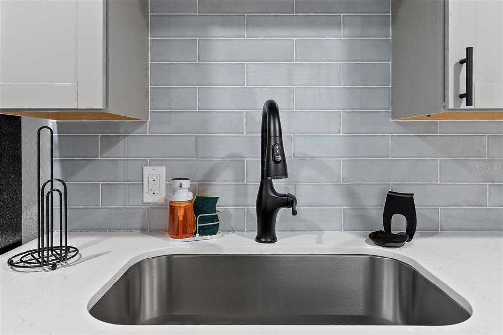A stainless steel kitchen sink features a black faucet against a light blue subway tile backsplash — 412 E HARWOOD STREET UNIT 2, ORLANDO, FL