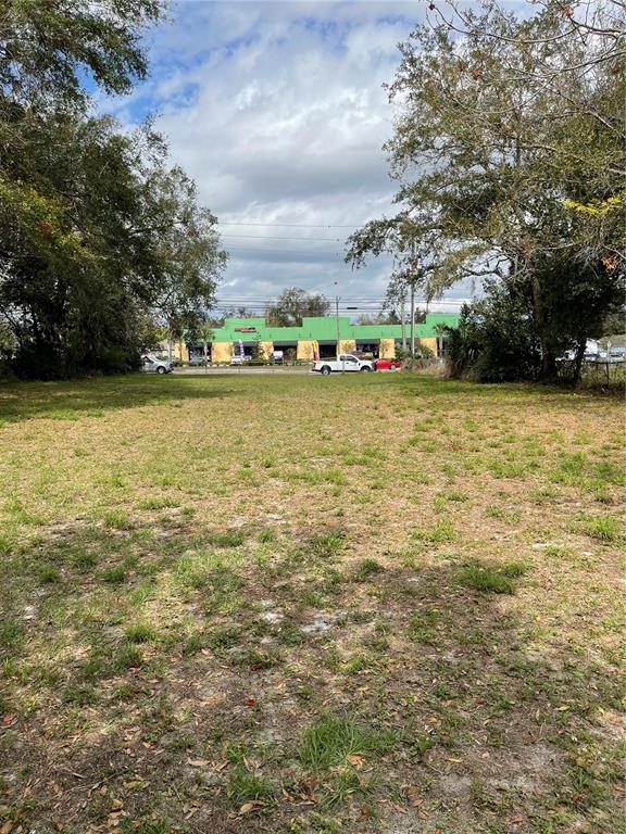 A vacant, grassy lot framed by trees with a commercial building visible in the background — 5910 OLD WINTER GARDEN ROAD, ORLANDO, FL