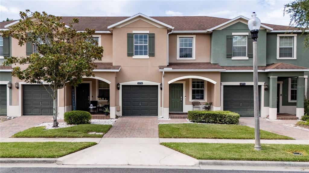 A row of three attached townhomes with tan and green stucco facades and attached garages — 10709 SAVANNAH LANDING CIRCLE, ORLANDO, FL