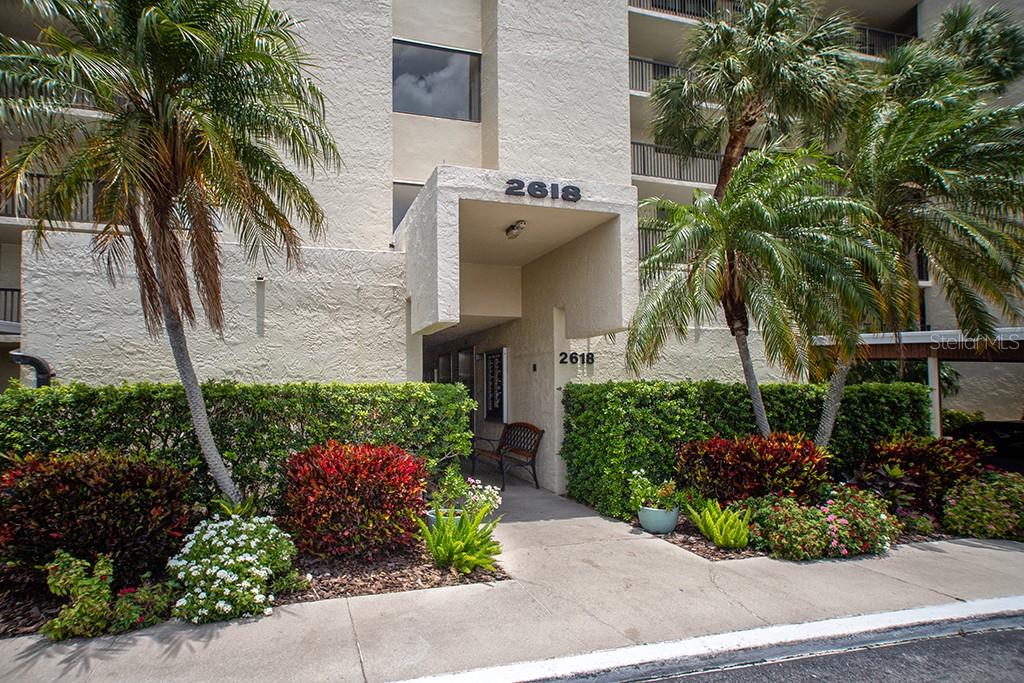 The exterior entrance of a multi-story residential building features a concrete walkway and landscaping — 2618 COVE CAY DRIVE UNIT 505, CLEARWATER, FL