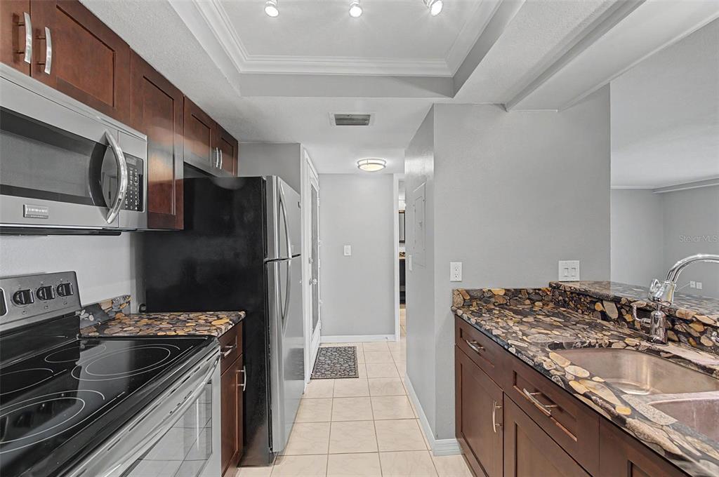 A kitchen features dark wood cabinets, black appliances, and patterned stone countertops — 2618 COVE CAY DRIVE UNIT 505, CLEARWATER, FL