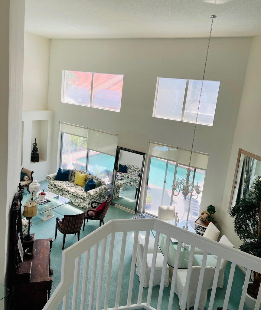A high-angle view of a living room with vaulted ceilings, carpet, and pool views — 17275 Ventana Drive, Boca Raton FL 33487, BOCA RATON, FL