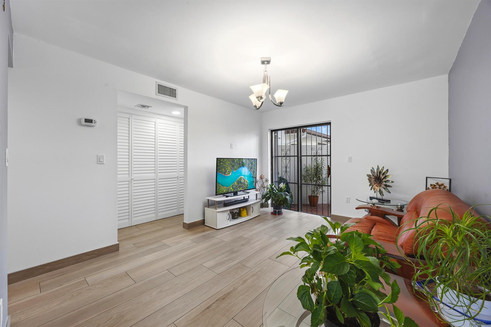 A living room with light wood-look flooring, white walls, a television, and a sliding door — 1461 SW 124th Court # c, Miami FL 33184, MIAMI, FL