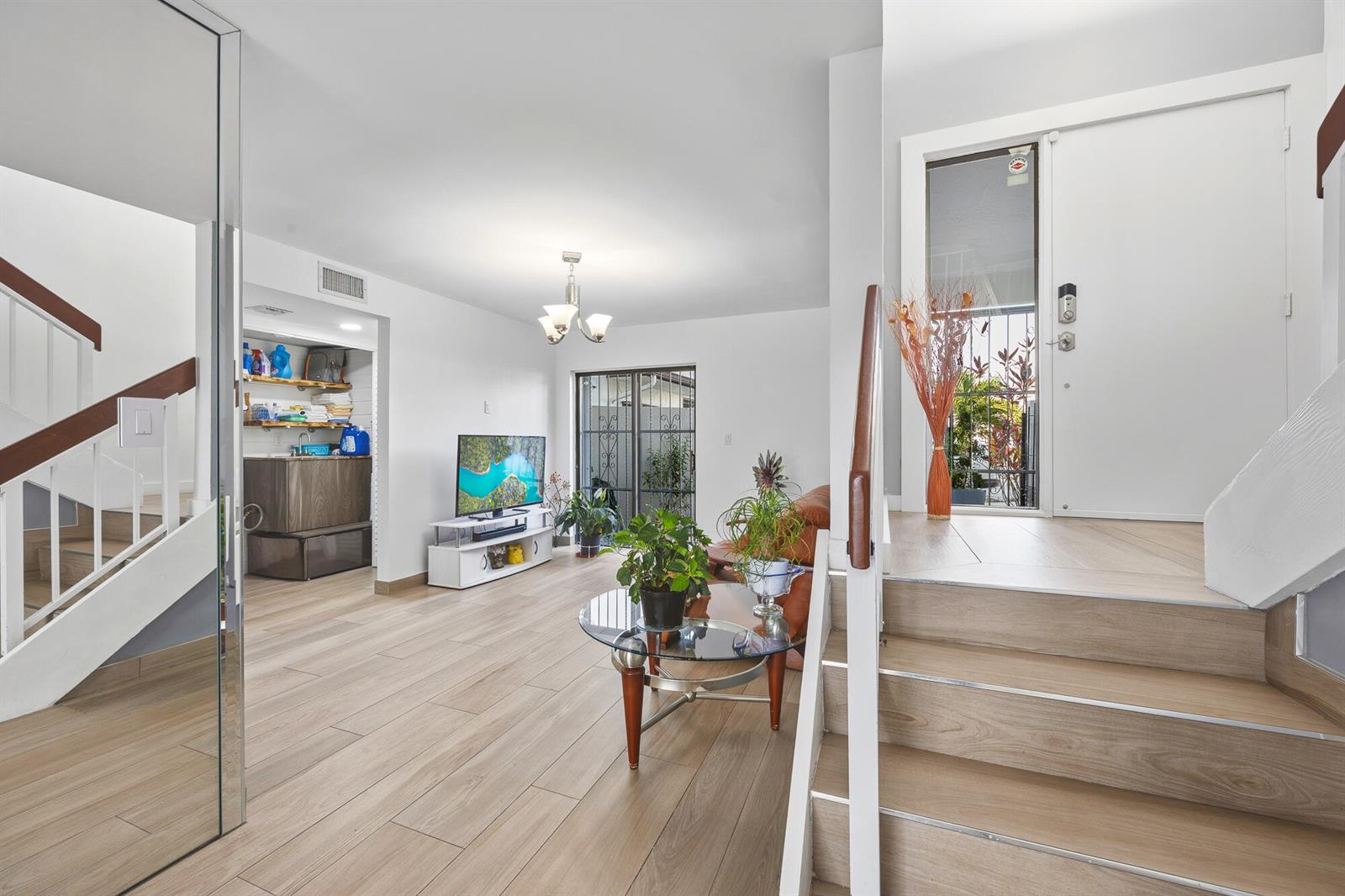 A living room features light wood-look flooring, a staircase, a television, and a glass door — 1461 SW 124th Court # c, Miami FL 33184, MIAMI, FL