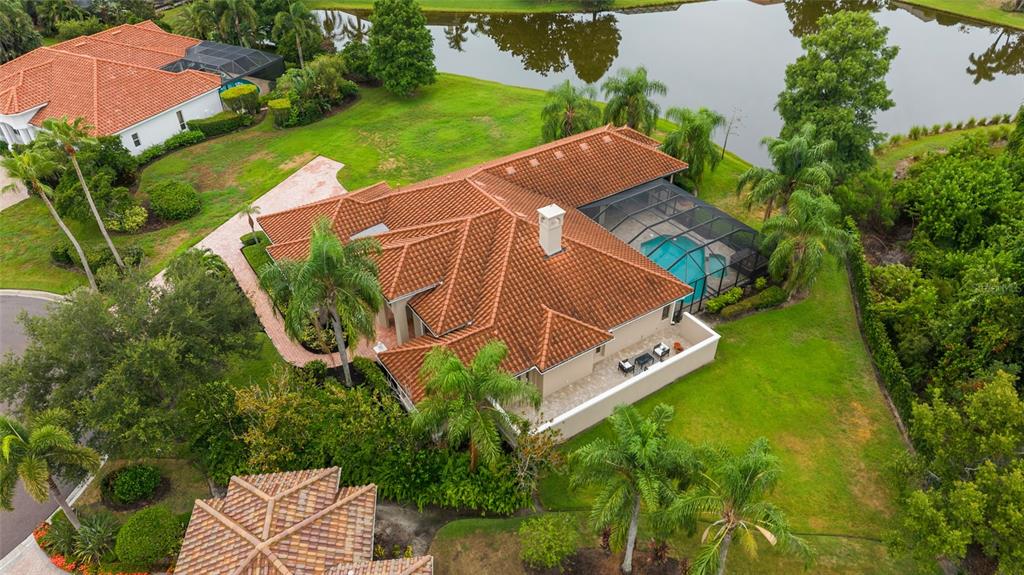An aerial view of a house with a tiled roof, pool enclosure, and backyard pond — 7808 DERBY CT, LAKEWOOD RANCH, FL
