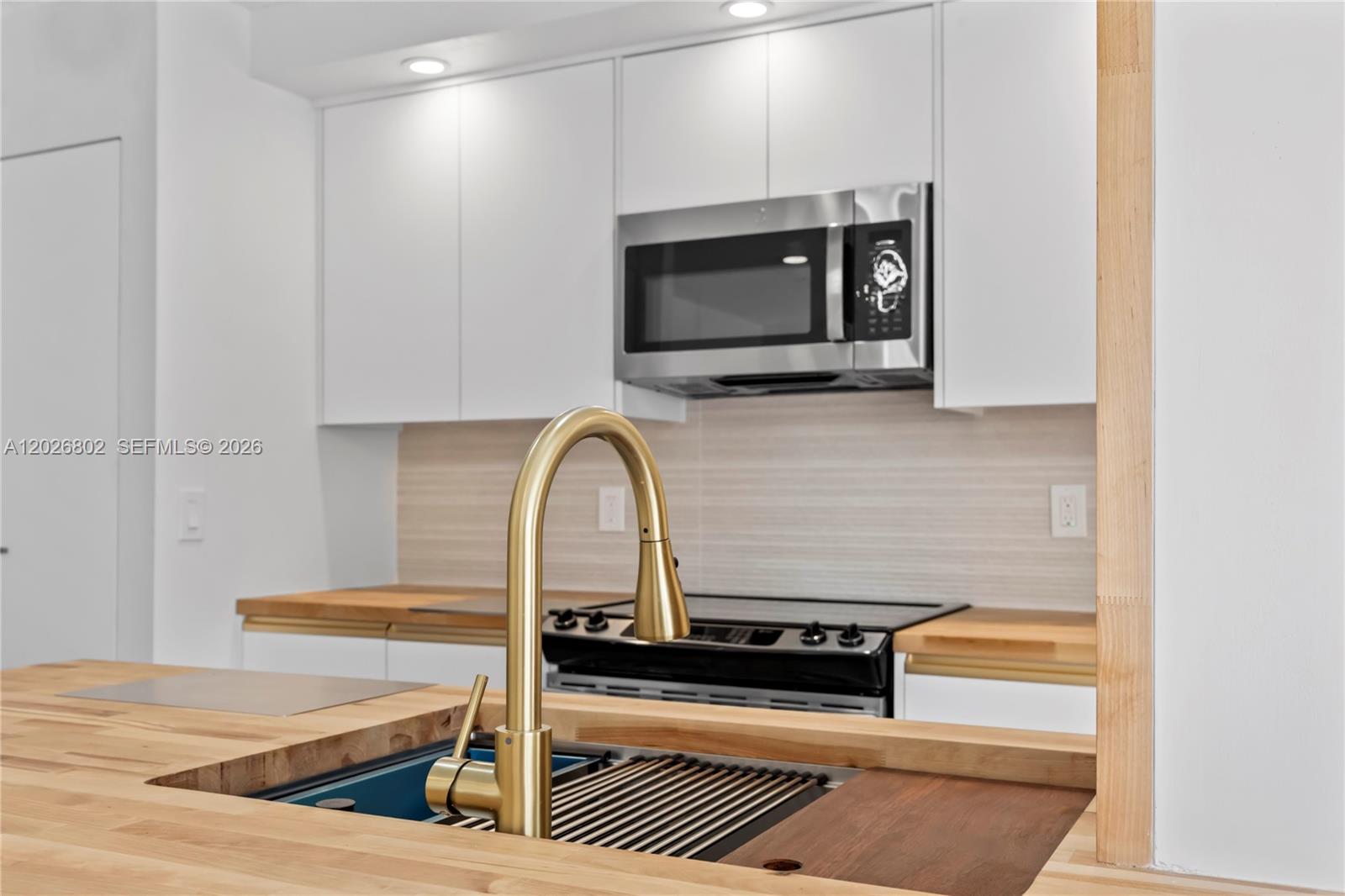 A kitchen features white cabinets, a wood countertop, and a gold faucet over a sink — 7511 S Oriole Blvd # 201, Delray Beach FL 33446, DELRAY BEACH, FL