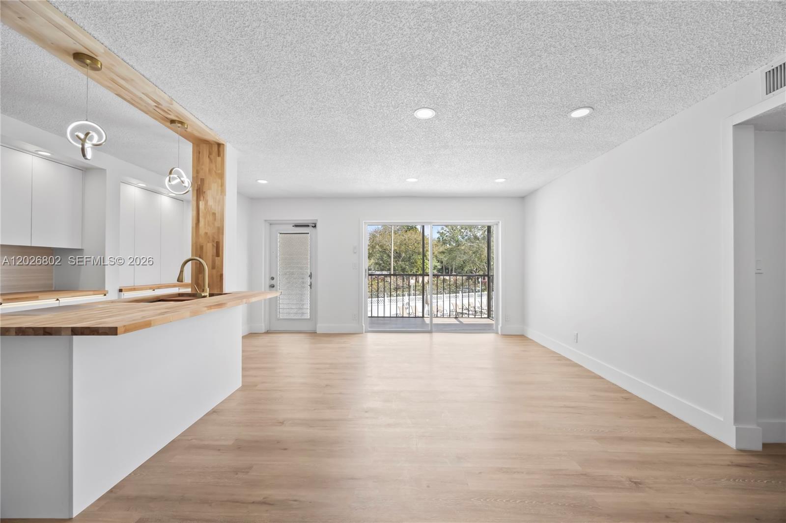 An open-concept living area features light wood flooring, a kitchen island, and a balcony door — 7511 S Oriole Blvd # 201, Delray Beach FL 33446, DELRAY BEACH, FL