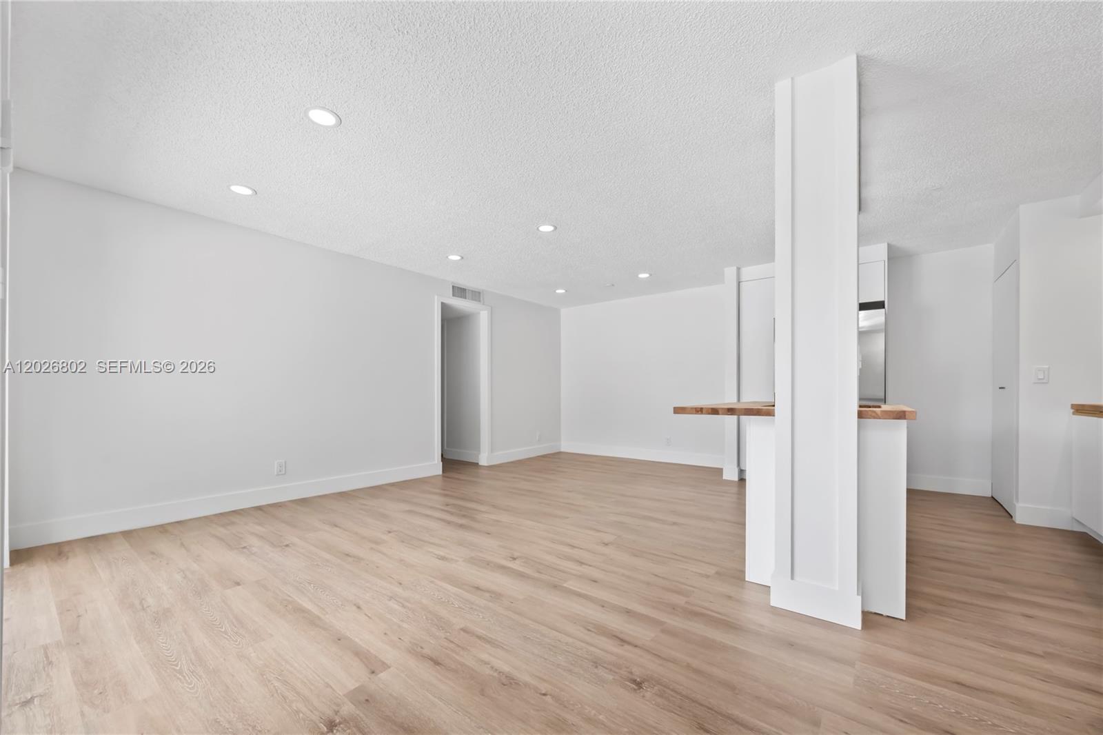 An open-concept living area features light wood-look flooring, white walls, and a central support column — 7511 S Oriole Blvd # 201, Delray Beach FL 33446, DELRAY BEACH, FL