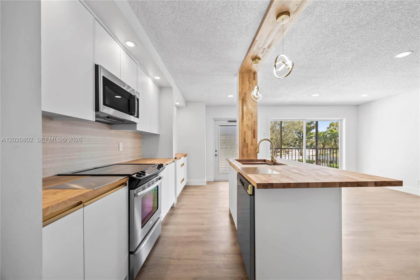 A modern kitchen features white cabinetry, wood countertops, a central island, and stainless steel appliances — 7511 S Oriole Blvd # 201, Delray Beach FL 33446, DELRAY BEACH, FL