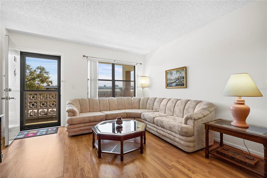 A living room features a large beige sectional sofa, a glass-topped coffee table, and wood flooring — 4910 BAY STREET NE UNIT 311, ST PETERSBURG, FL