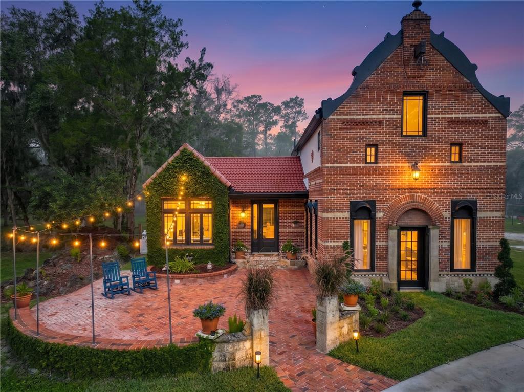 A brick house with a red tile roof and a patio featuring string lights at dusk — 2291 WACCASSA STREET, GENEVA, FL