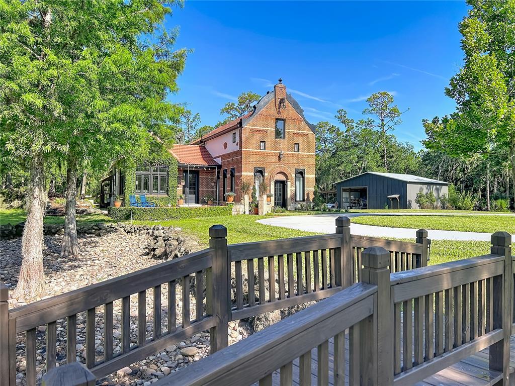 A brick house with a gabled roof stands behind a wooden bridge and lawn — 2291 WACCASSA STREET, GENEVA, FL
