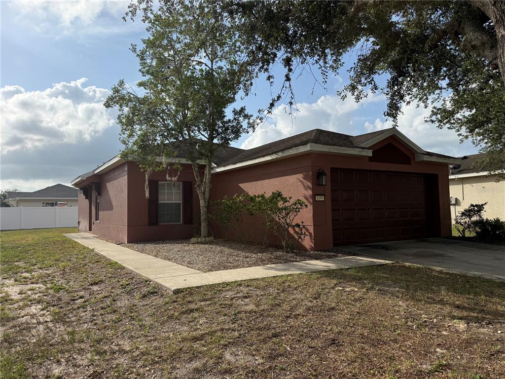 A single-story house with a reddish-brown stucco exterior, a two-car garage, and a front tree — 1188 THREE LEAF LANE, BROOKSVILLE, FL
