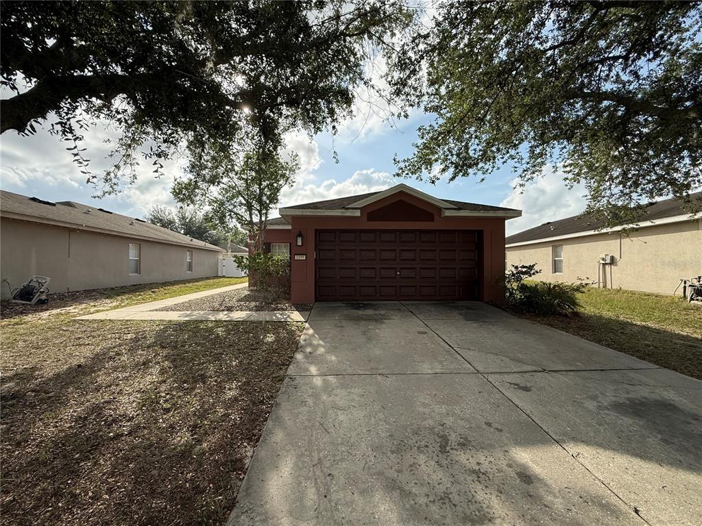 A single-story house with a brown garage door and a concrete driveway under large trees — 1188 THREE LEAF LANE, BROOKSVILLE, FL