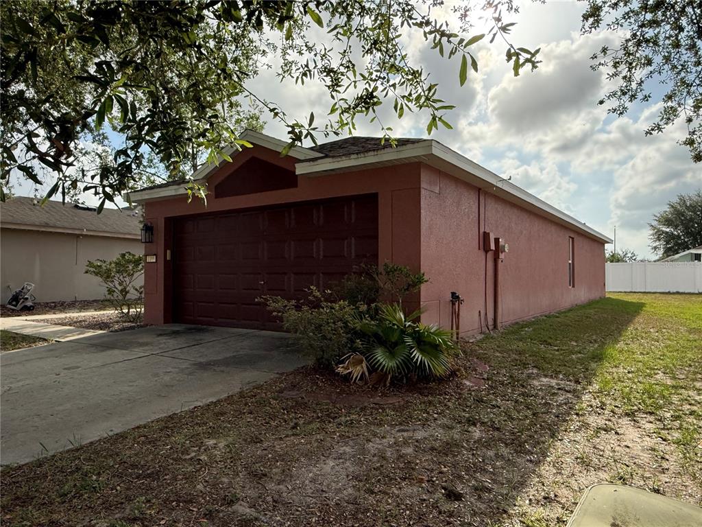 The exterior of a single-story house features a dark brown garage door and stucco walls — 1188 THREE LEAF LANE, BROOKSVILLE, FL