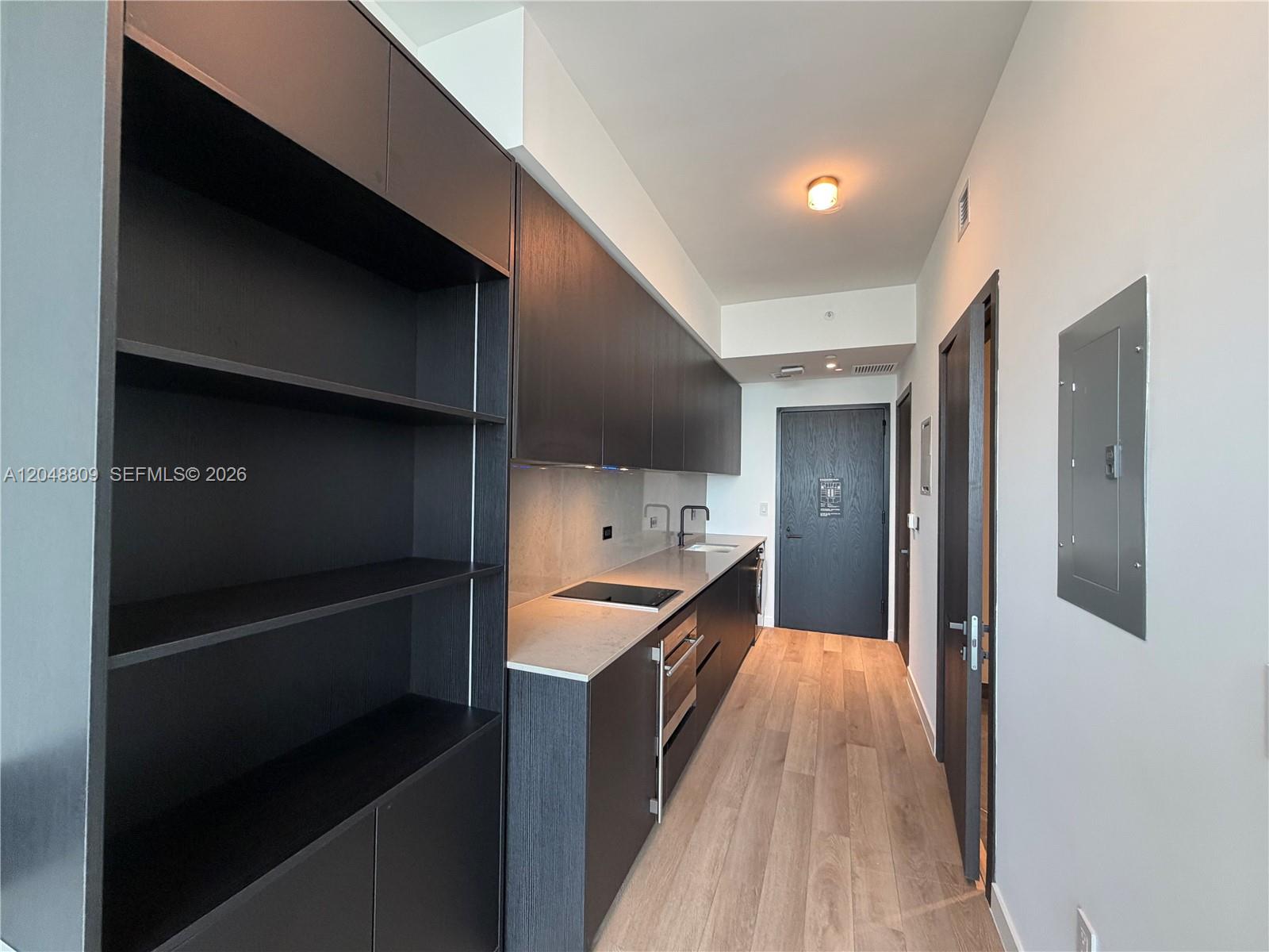A galley kitchen features dark wood cabinetry, light countertops, and light wood flooring — 20 NE 11th # 2703B, Miami FL 33132, MIAMI, FL