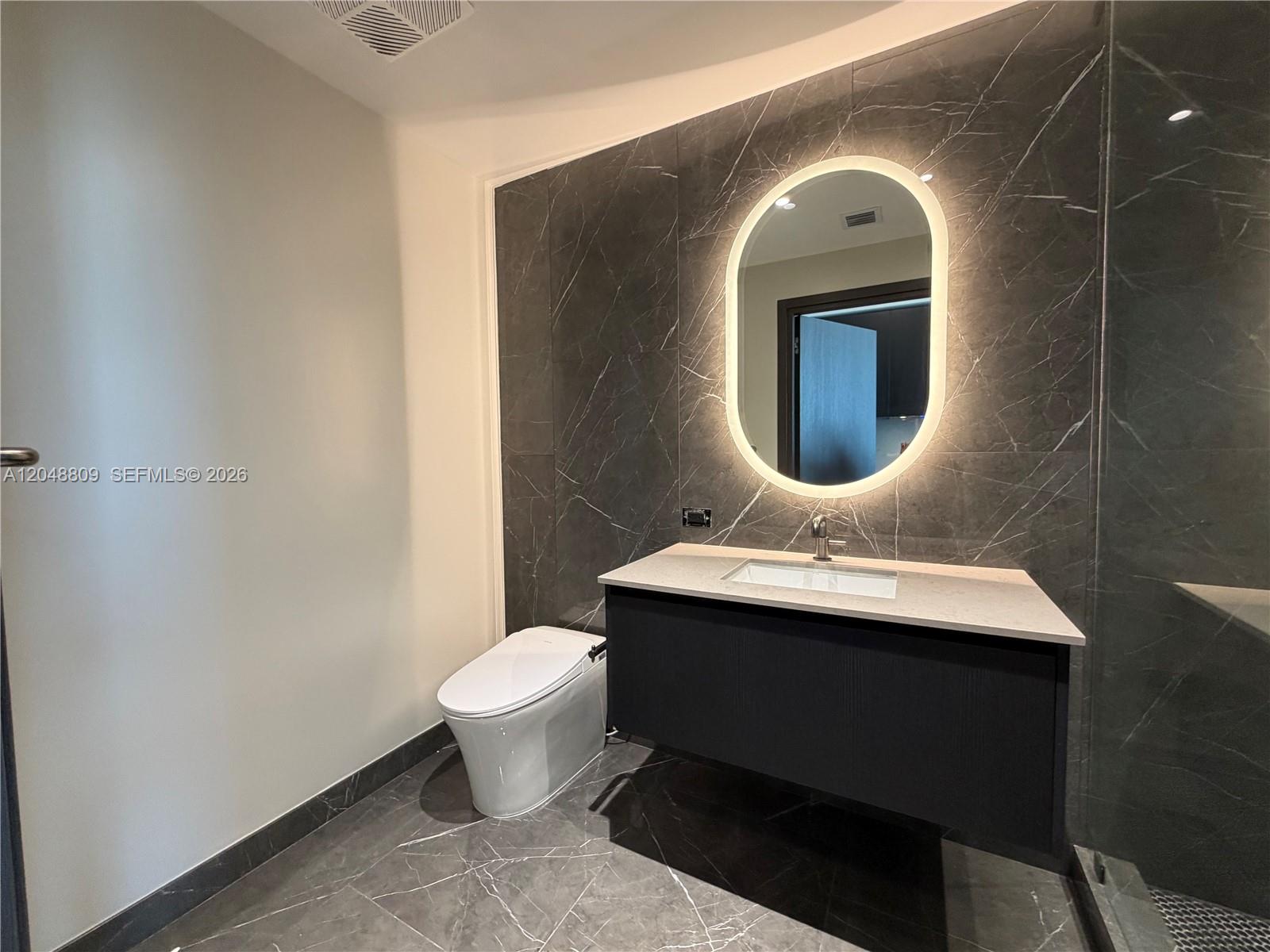 A modern bathroom features a floating vanity, a backlit oval mirror, and dark marble tiling — 20 NE 11th # 2703B, Miami FL 33132, MIAMI, FL