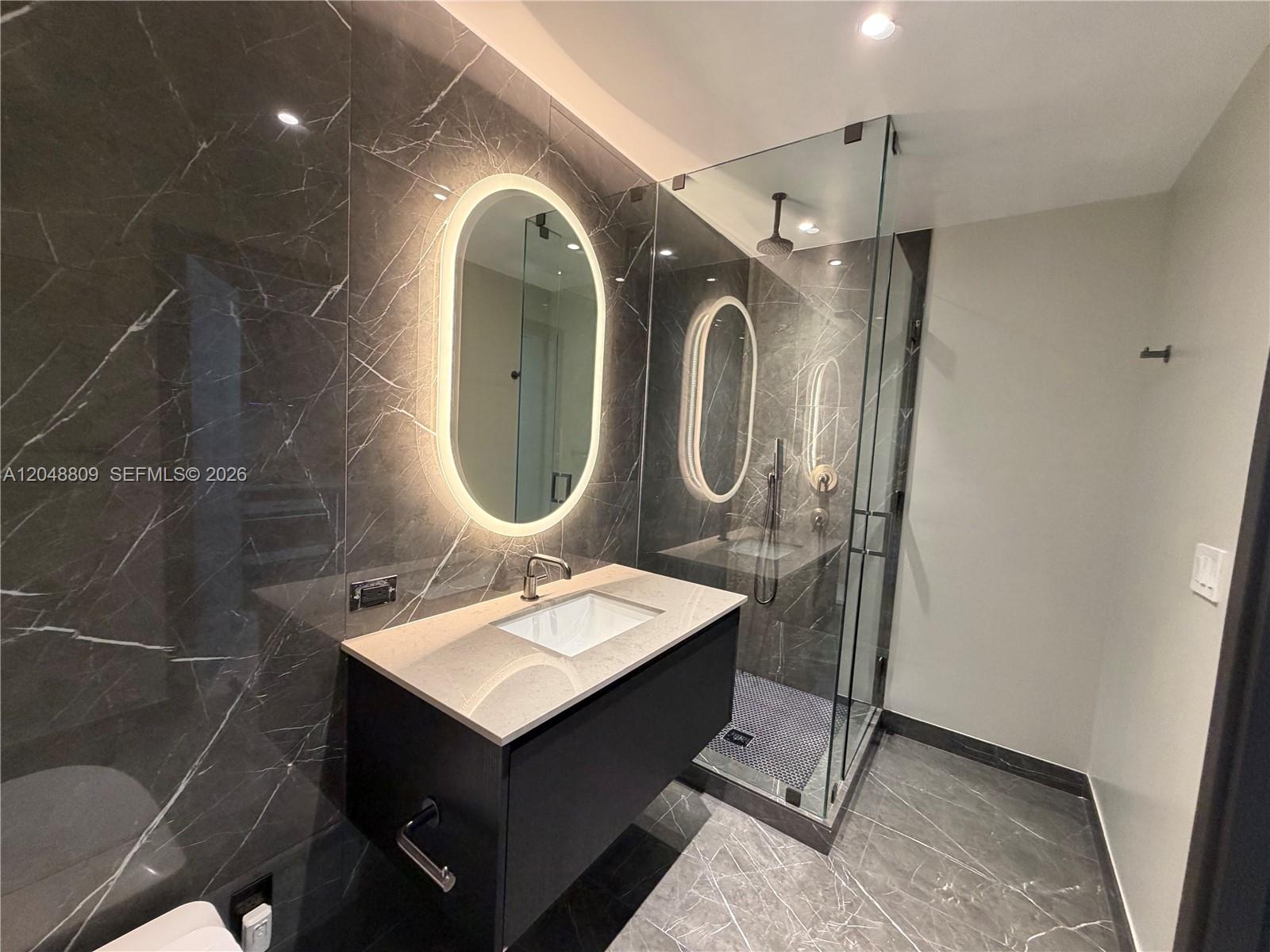A modern bathroom features a floating vanity, an illuminated oval mirror, and a glass shower — 20 NE 11th # 2703B, Miami FL 33132, MIAMI, FL