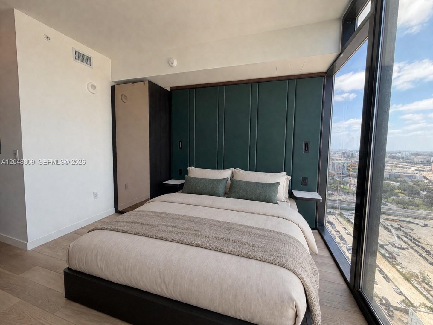 A bedroom features a green upholstered headboard, a platform bed, and floor-to-ceiling windows — 20 NE 11th # 2703B, Miami FL 33132, MIAMI, FL