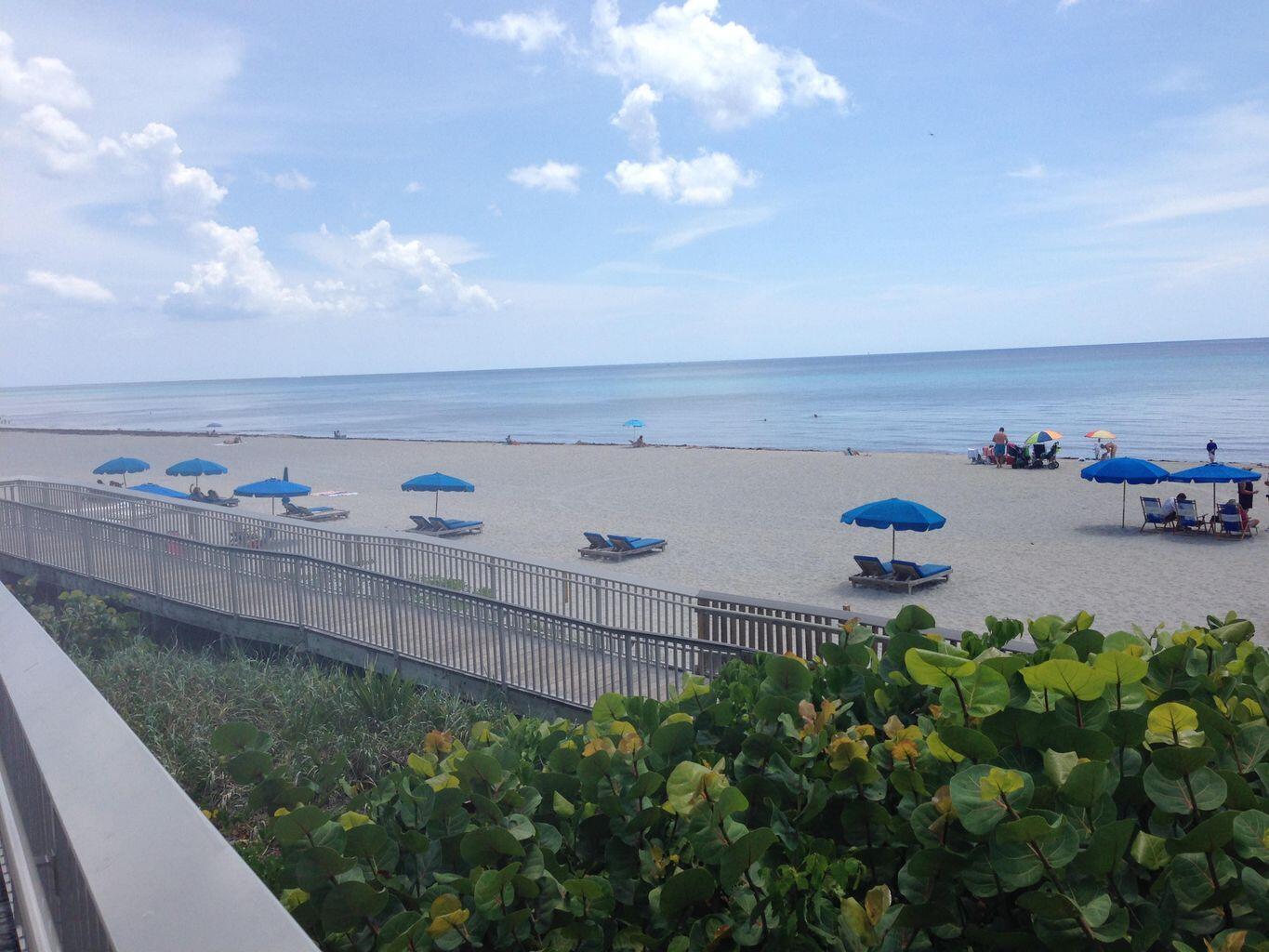 A view of a sandy beach with blue umbrellas and lounge chairs from a boardwalk — 6520 N Ocean Boulevard # 3, Ocean Ridge FL 33435, OCEAN RIDGE, FL