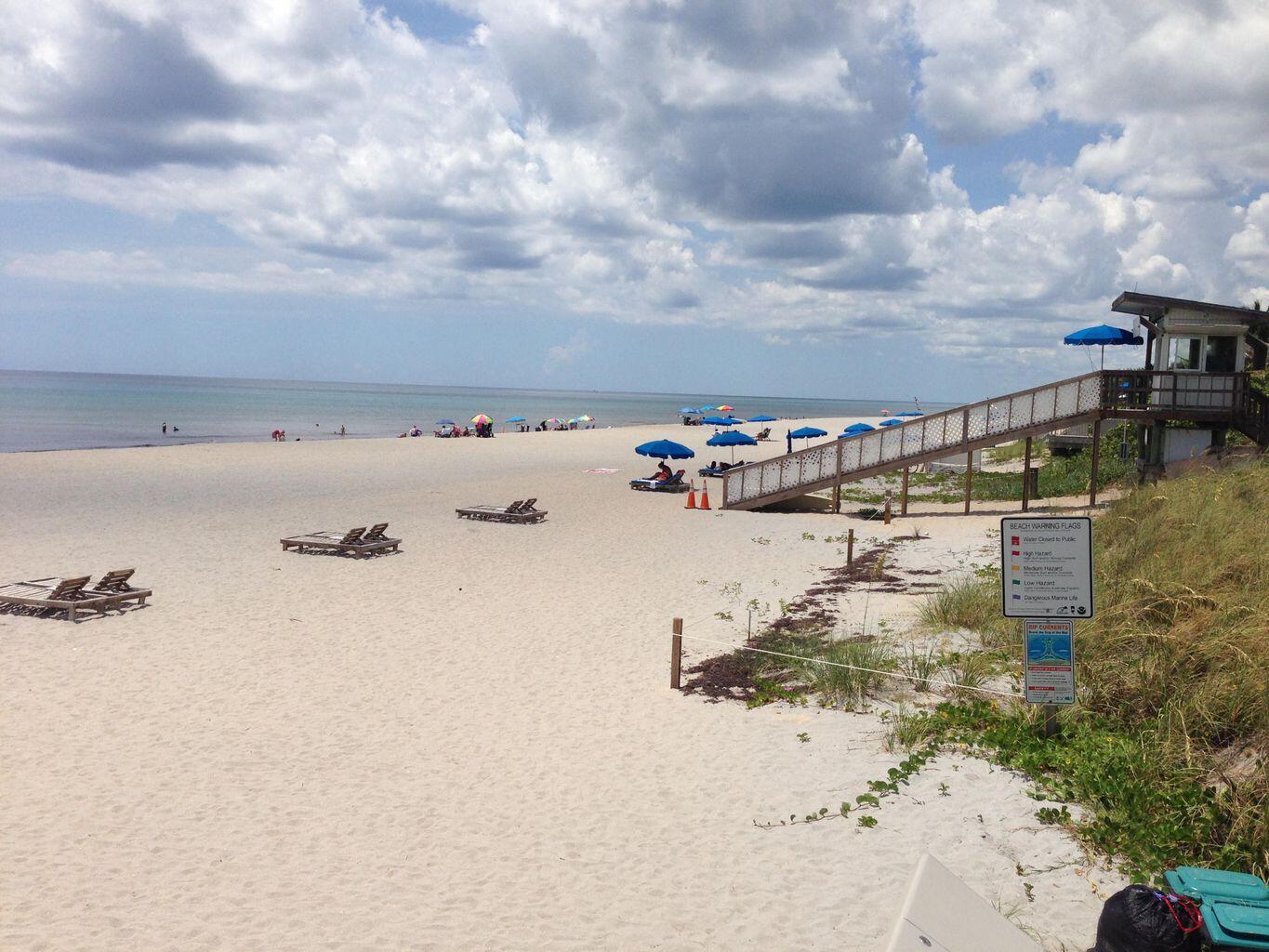 A sandy beach with lounge chairs, blue umbrellas, a wooden staircase, and a lifeguard tower — 6520 N Ocean Boulevard # 3, Ocean Ridge FL 33435, OCEAN RIDGE, FL