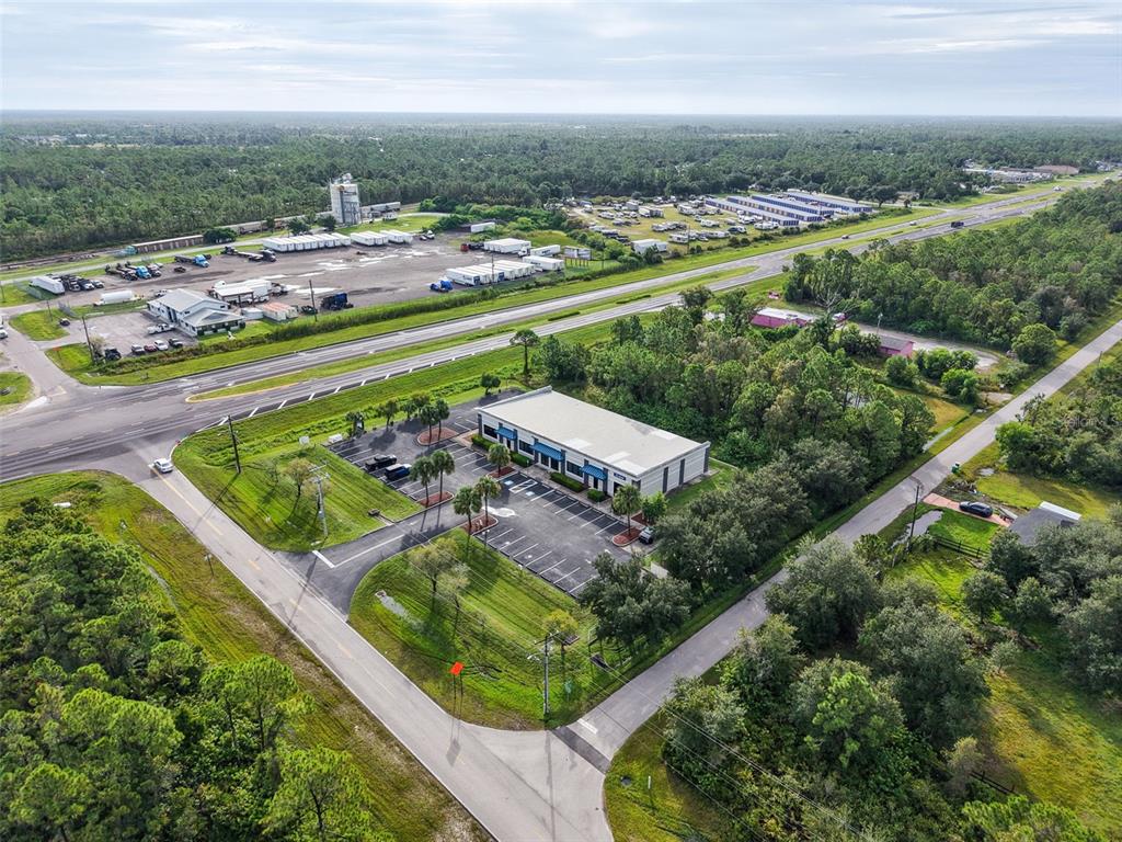 An aerial view shows a commercial building with a parking lot surrounded by wooded land — 29291 TRIBUNE BOULEVARD UNIT 4-109, PUNTA GORDA, FL