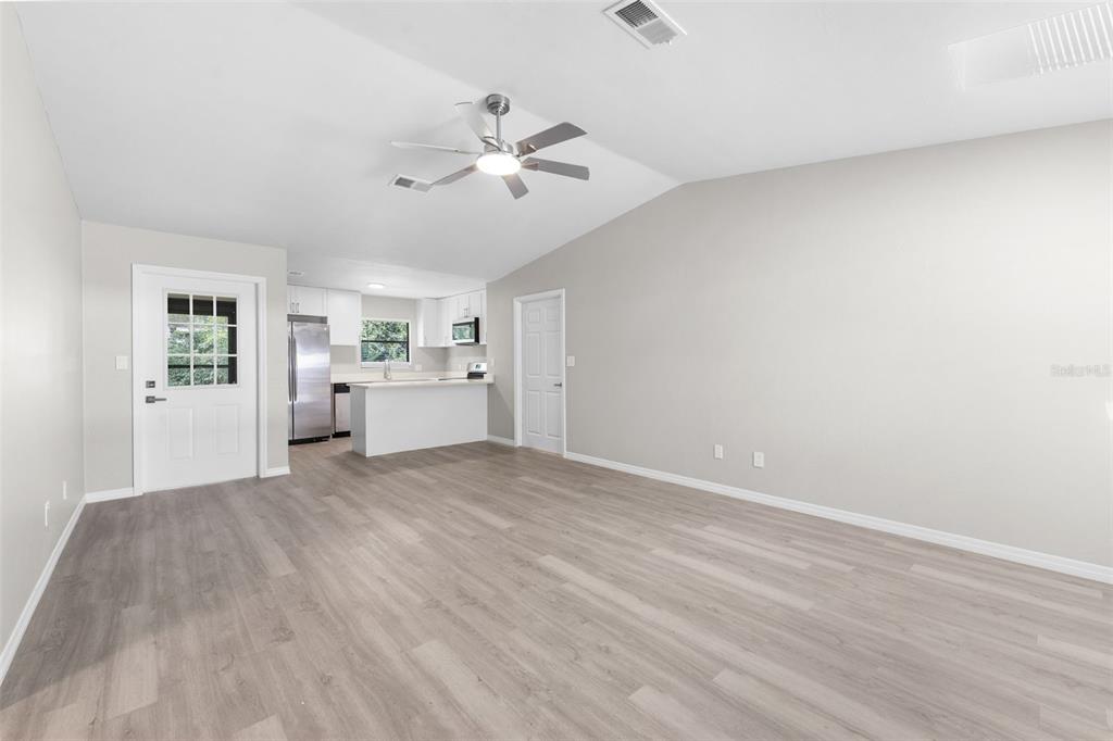 A bright, open-concept living area features light gray walls, wood-look flooring, and a kitchen island — 2329 NW 54TH PLACE, GAINESVILLE, FL