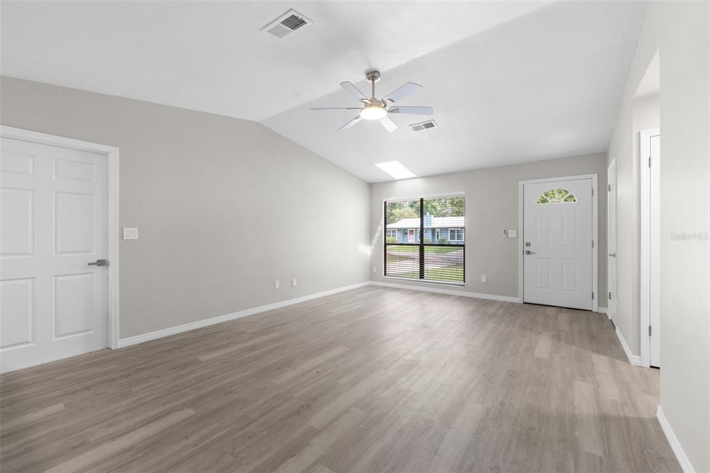 An empty living room features light gray walls, wood-look flooring, a ceiling fan, and a door — 2329 NW 54TH PLACE, GAINESVILLE, FL
