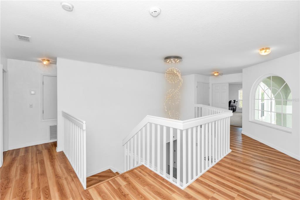 A second-floor landing with wood-look flooring, a white railing, and a modern spiral chandelier — 219 STRATHMORE CIRCLE, KISSIMMEE, FL