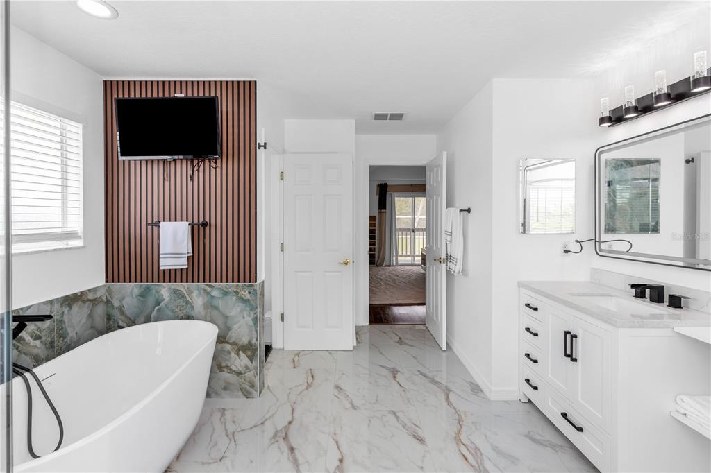 A modern bathroom features a freestanding tub, marble-look tile flooring, and a wood-slat accent wall — 219 STRATHMORE CIRCLE, KISSIMMEE, FL