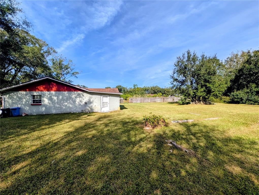 A side view of a single-story house with a large, grassy backyard and trees — 8410 PETERSON ROAD, ODESSA, FL