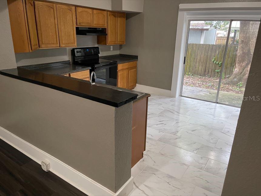 A kitchen with wood cabinets, black countertops, and white tile flooring leads to a sliding door — 590 S BROADWAY AVENUE, BARTOW, FL