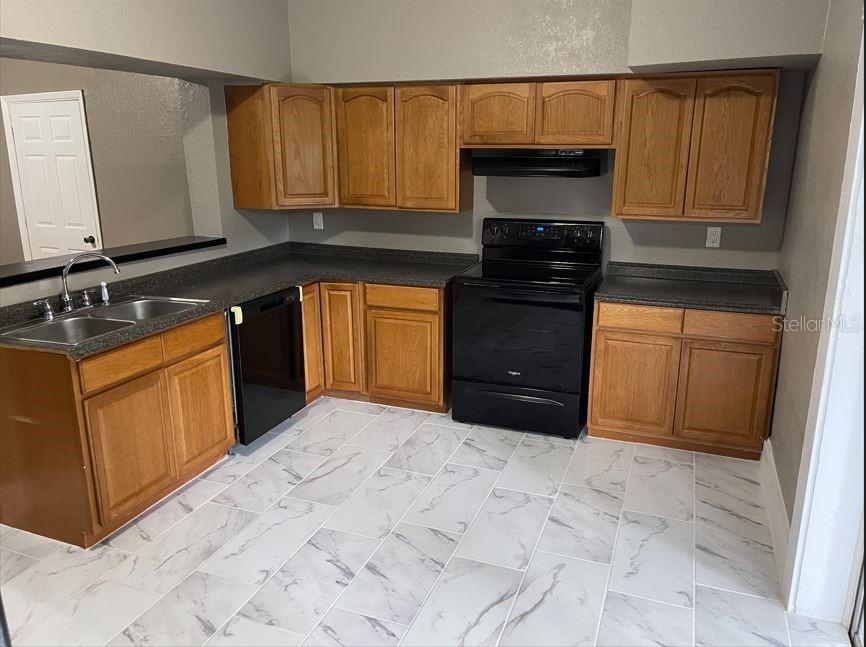 A kitchen with wood cabinets, black appliances, dark countertops, and white marble-patterned tile flooring — 590 S BROADWAY AVENUE, BARTOW, FL