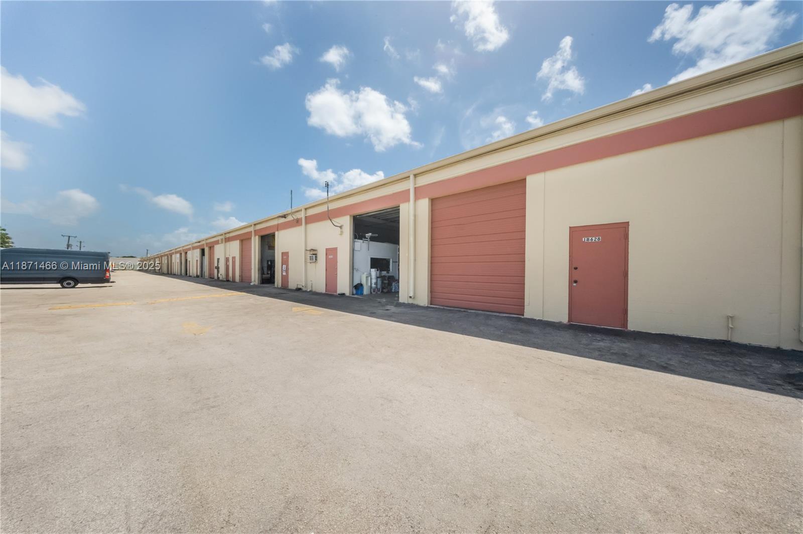 An exterior view of a long industrial warehouse building with multiple roll-up doors and entry doors — 18625 SW 105 AV, Miami FL 33157, MIAMI, FL
