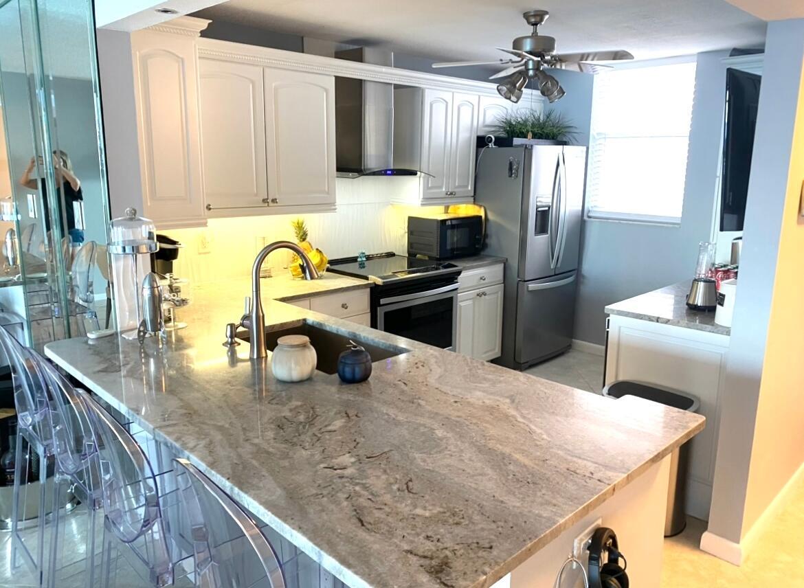 A kitchen features white cabinets, granite countertops, stainless steel appliances, and a breakfast bar — 9940 S Ocean Drive # 1004, Jensen Beach FL 34957, JENSEN BEACH, FL