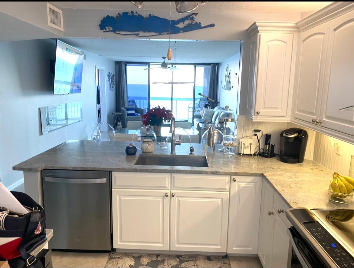 A kitchen with white cabinets and granite countertops overlooks a living area with ocean views — 9940 S Ocean Drive # 1004, Jensen Beach FL 34957, JENSEN BEACH, FL
