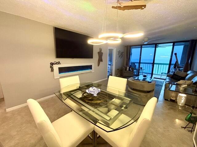 A dining area with a glass table and fireplace sits before a living room with ocean views — 9940 S Ocean Drive # 1004, Jensen Beach FL 34957, JENSEN BEACH, FL