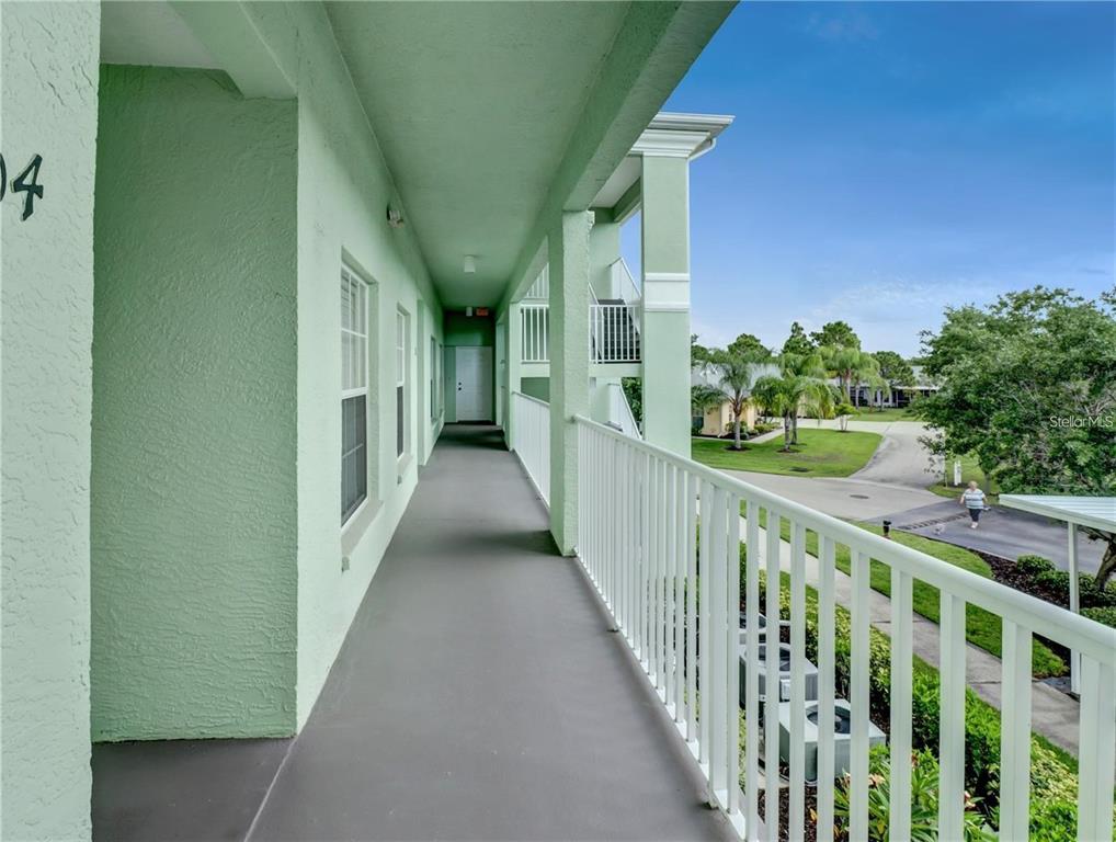 An outdoor covered walkway with light green walls and a white metal railing — 2121 HERON LAKE DRIVE UNIT 204, PUNTA GORDA, FL