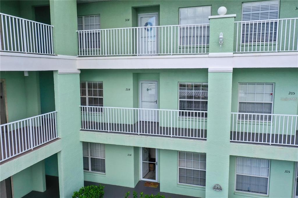 An exterior view of a three-story apartment building with green stucco walls and white railings — 2121 HERON LAKE DRIVE UNIT 204, PUNTA GORDA, FL