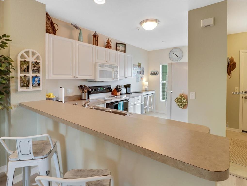 A kitchen with white cabinets, a beige countertop, and a breakfast bar with stools — 2121 HERON LAKE DRIVE UNIT 204, PUNTA GORDA, FL