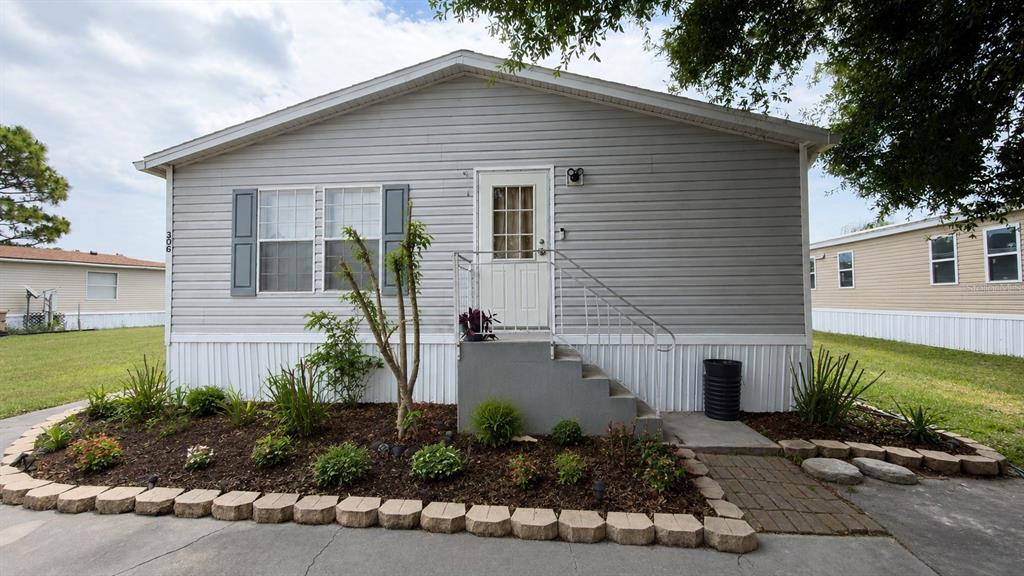 A gray manufactured home features a front entrance with concrete steps and a landscaped garden — 306 EVANDEE COURT, KISSIMMEE, FL
