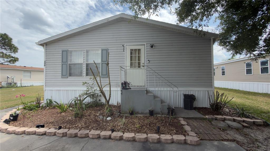 A gray manufactured home features a front entrance with concrete steps and a landscaped garden — 306 EVANDEE COURT, KISSIMMEE, FL