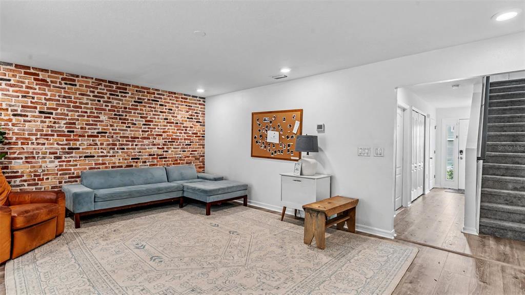 A living room features a brick accent wall, a blue sectional sofa, and wood flooring — 3806 EXETER LANE, LAKELAND, FL