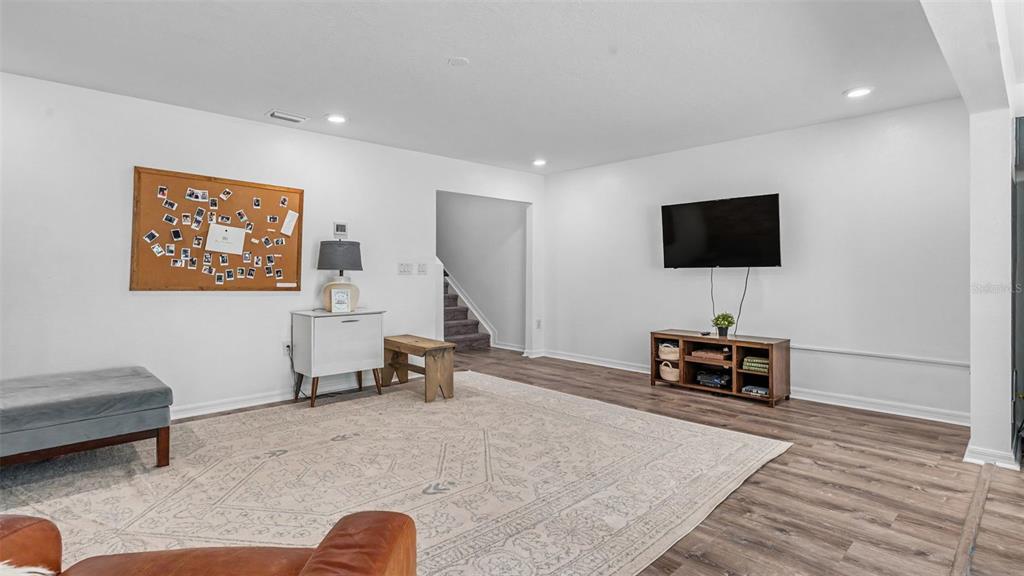 A living room with white walls, wood-look flooring, a large area rug, and a television — 3806 EXETER LANE, LAKELAND, FL