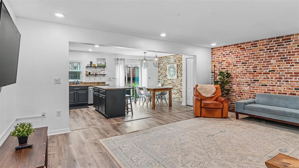 An open-concept living and dining area features a brick accent wall and wood-look flooring — 3806 EXETER LANE, LAKELAND, FL