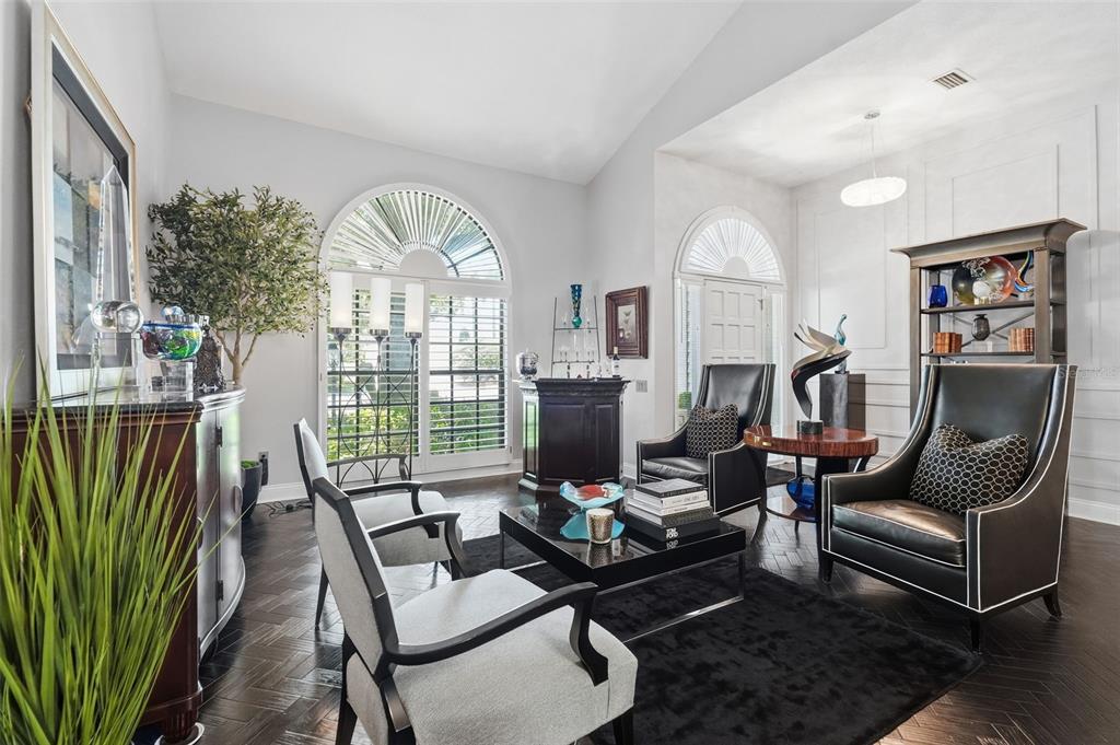 A living room features dark herringbone wood floors, arched windows, and a mix of seating — 11760 ASHLEY COURT, SEMINOLE, FL