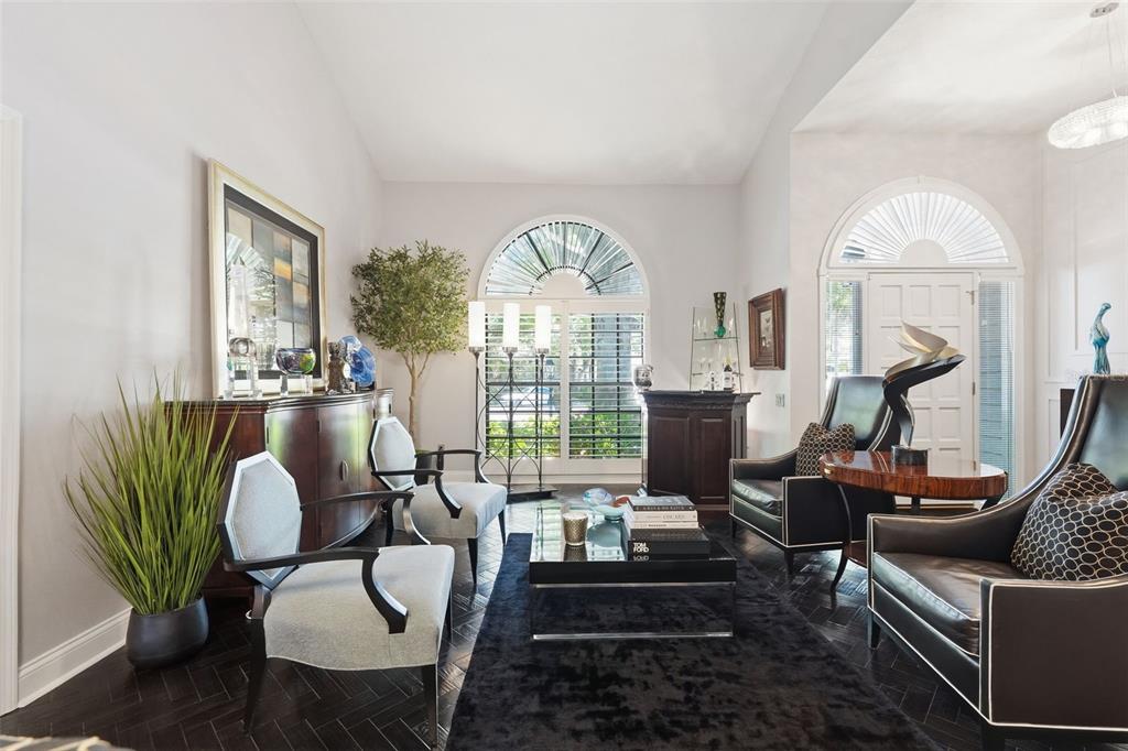 A formal living room features dark herringbone floors, arched windows, and a mix of seating — 11760 ASHLEY COURT, SEMINOLE, FL