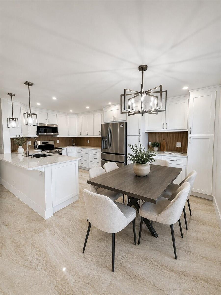 A modern kitchen and dining area features white cabinetry, a marble island, and wood-toned backsplash — 4047 Ainslie C # 4047, Boca Raton FL 33434, BOCA RATON, FL